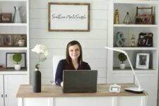 a cute white modern country home office with a planked wall, built-in storage units, a large desk and a neutral chandelier