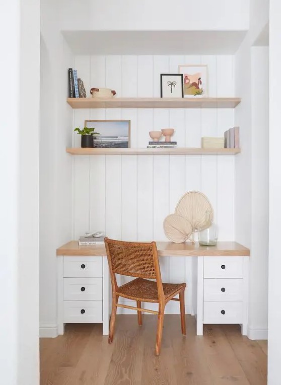 a deep white niche with shiplap, built-in shelves and a large desk with drawers, some books and decor and a cane chair