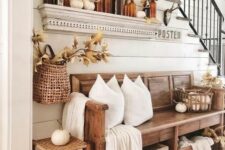 a fall farmhouse entryway with a wooden bench, a woven stool, pillows and a blanket, amber bottles and lots of leaves