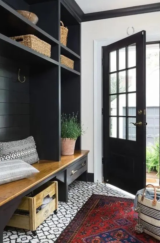 a farmhouse black and white entryway with a printed tile floor, a black storage unit with baskets, a bench and some potted plants
