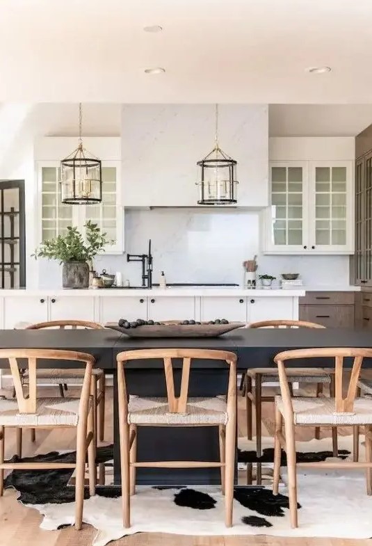 a farmhouse dining space with a black dining table, stained wishbone chairs, a cowhide rug and a kitchen zone next to it