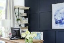 a farmhouse home office with a navy paneled wall, a bold artwork, a wooden desk and a basket plus a storage unit