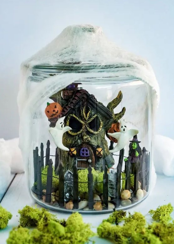 a fun Halloween terrarium with a mini funky graveyard, a witch, some ghosts, jack-o-lanterns and pebbles