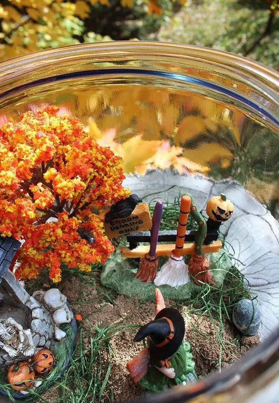 a fun Halloween terrarium with a witch, a fall tree, jac-o-lanterns, skulls and bones and brooms at a stand