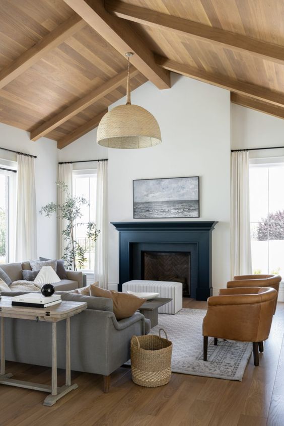 a laconic modern farmhouse living room with a fireplace with a black mantel, a coffee table, grey and beige sofas, amber leather chairs and a woven pendant lamp