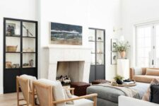 a light-filled modern farmhouse living room with a fireplace, built-in storage units, a grey ottoman, neutral seating furniture and a chandelier