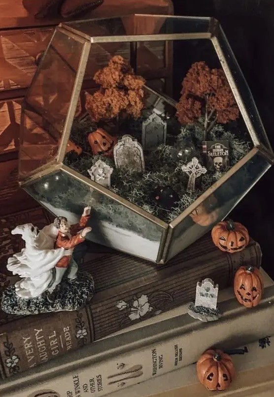 a lovely Halloween terrarium with moss, tombstones, jack o lanterns, fall trees and a graveyard