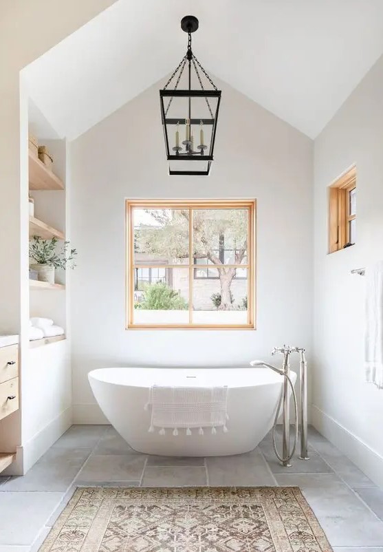 a lovely modern farmhouse bathroom with built in shelves, a timber vanity, an oval tub, a couple of windows with stained frames
