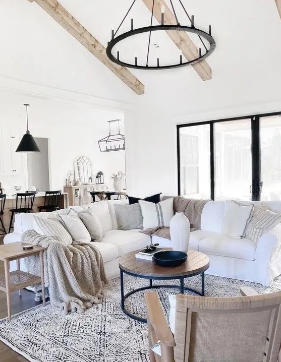 a lovely modern farmhouse living room with wooden beams on the ceiling, a white sectional, a coffee table, some chairs and tables