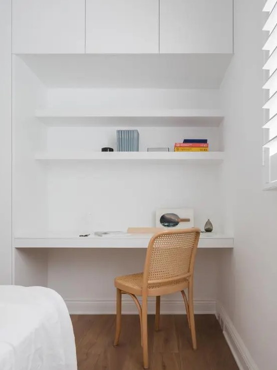 a minimalist niche with built-in shelves and a desk, some books and a cane chair is a lovely nook to squeeze into a bedroom