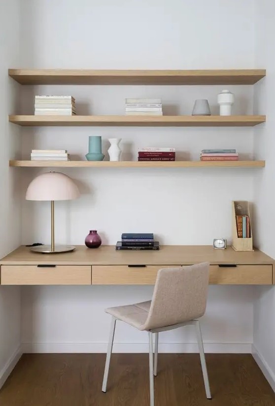a minimalist niche with built in shelves and a desk with drawers, a neutral chair, a table lamp and some books