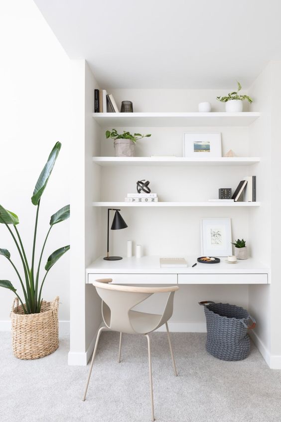 a minimalist white niche with built-in shelves and a sleek desk with drawers, some potted plants, books and baskets
