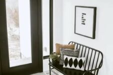 a modern black and white foyer with a black glass door, a black bench and a striped rug, an artwork and lanterns