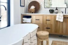a modern country bathroom with herringbone and hex tiles, an oval tub, a timber vanity, a wooden stool, a mirror and some decor