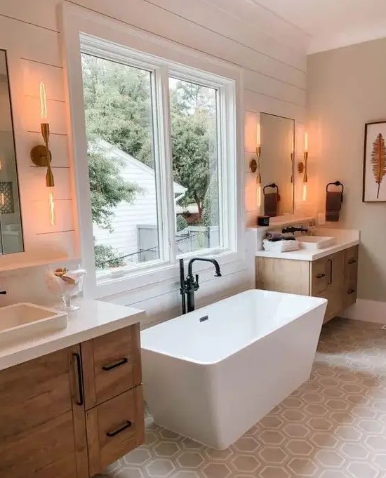 a modern country bathroom with white planked walls, a hexagon tile floor, wooden vanities, a modern tub and black fixtures