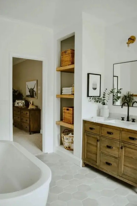 a modern country bathroom with white subway and hexagon tiles, a stained wooden vanity and built in shelves plus an oval tub
