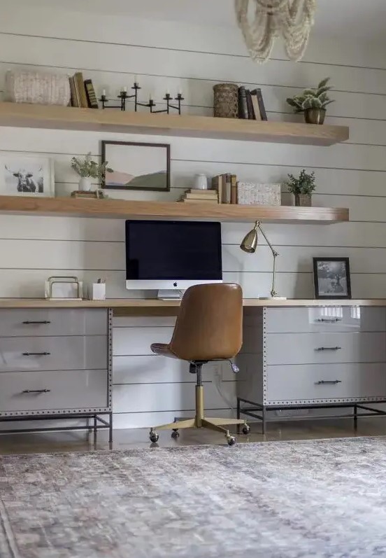 a modern country home office with a white planked wall, a grey desk, a leather chair, wooden slab floating shelves