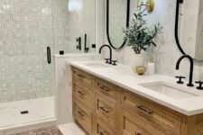 a modern farmhouse bathroom with printed and marble tile, a stained vanity, oval mirrors, black hardware and a boho rug