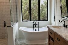 a modern farmhouse bathroom with subway and hex tiles, shiplap walls, a stained vanity, black lamps and a view of the forest