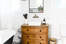 a modern farmhouse bathroom with white shiplap walls, a black printed tile floor, a vintage dresser vanity, a black tub and baskets