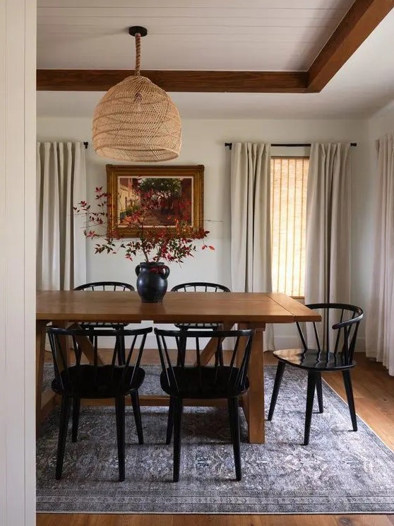 a modern farmhouse dining room with a stained table, black chairs, a woven pendant lamp and neutral textiles plus a lovely artwork