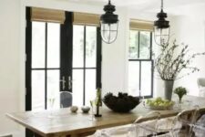 a modern farmhouse dining room with a wooden table, wicker shades, ghost chairs, vintage lanterns and black doors