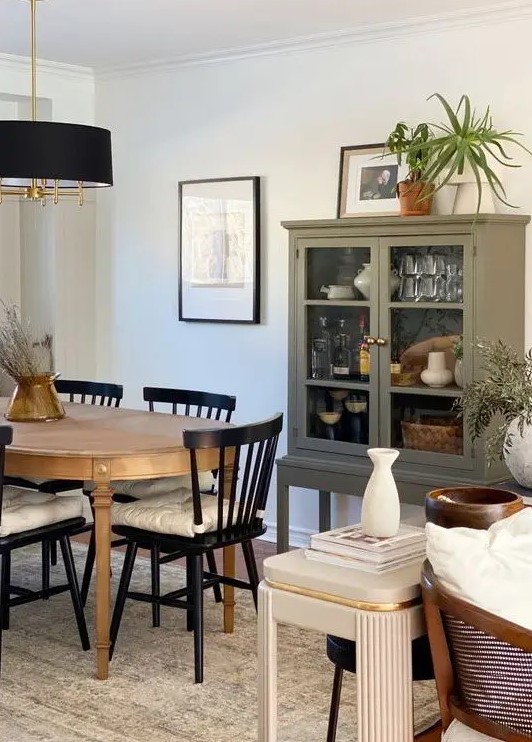 a modern farmhouse dining room with an olive green cupboard, an oval stained table, black farmhouse chairs, a black chandelier and some art and decor