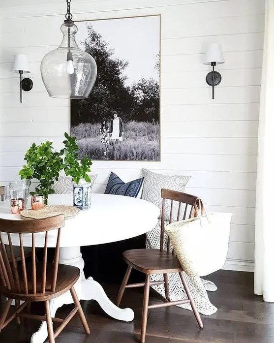 a modern farmhouse dining room with shiplap walls, a round table, a bench, stained chairs, a pendant lamp and wall sconces plus a large photo