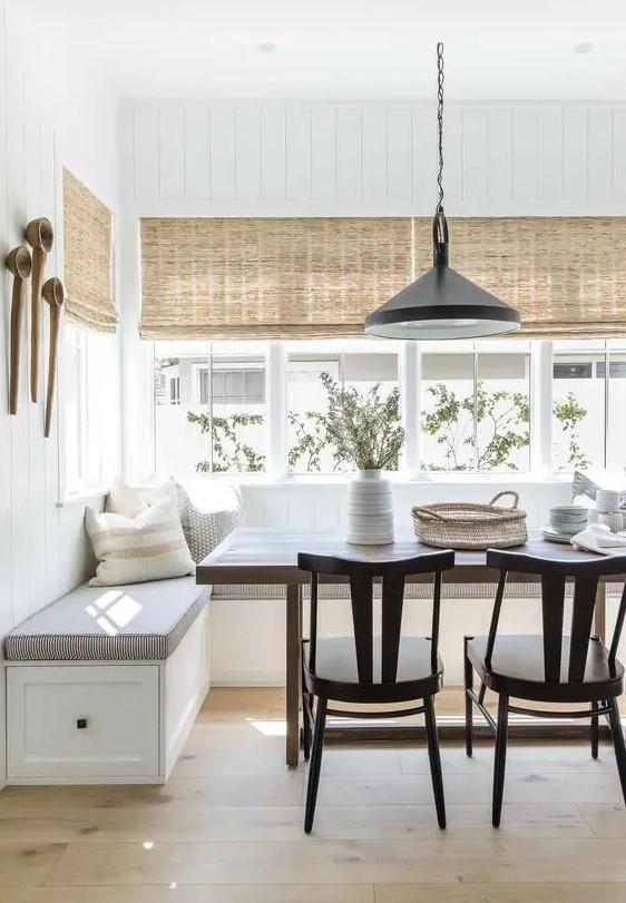 a modern farmhouse dining space with a corner banquette seating, a stained table and black chairs, a black pendant lamp