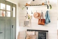 a modern farmhouse entry with a black bench, a basket, a shelf with some decor and greenery and some hooks