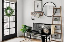 a modern farmhouse entry with a black bench, a ladder with wire baskets, a mirror and a rack, some greenery and a rug