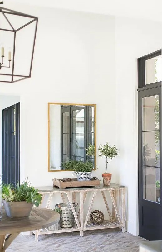a modern farmhouse entry with a brick floor, a console table with buckets and greenery, a stained table and a frame lamp