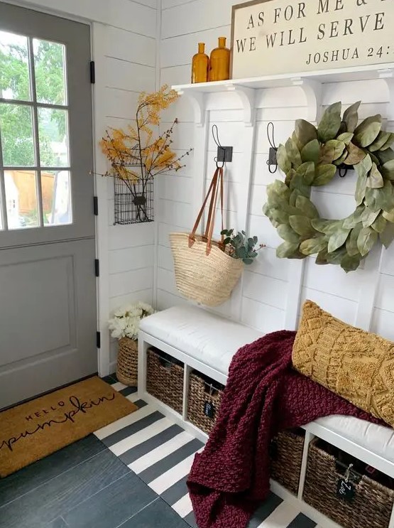 a modern farmhouse entryway with a built-in upholstered bench, a rack, some sings, greenery and leaves