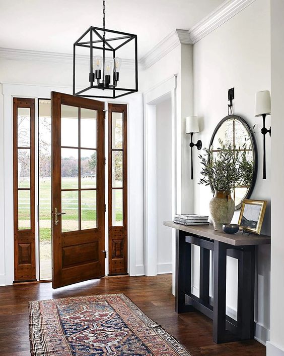 a modern farmhouse entryway with a pendant lamp, a console table with a mirror over it, greenery in a vase