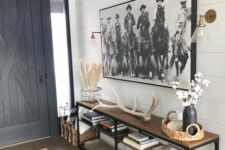 a modern farmhouse entryway with a tiered console table with antlers, dried flowers, an oversized artwork
