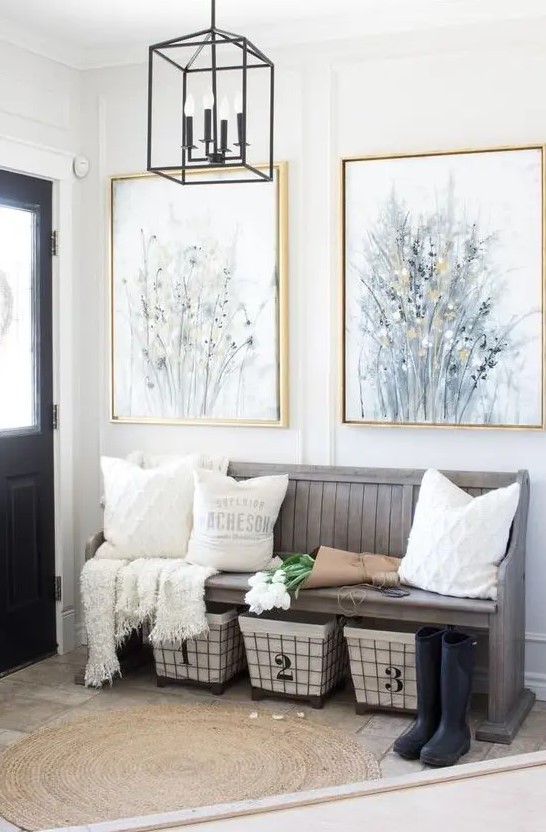 a modern farmhouse entryway with a weathered wood bench, wire baskets for storage, neutral pillows and artworks