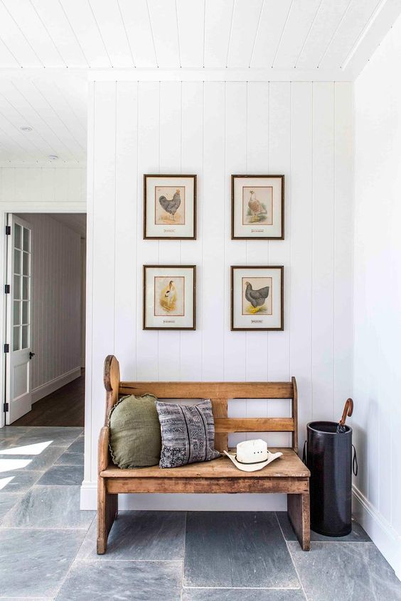 a modern farmhouse entryway with a wooden bench with pillows, a grid gallery wall, a bucket for umbrellas