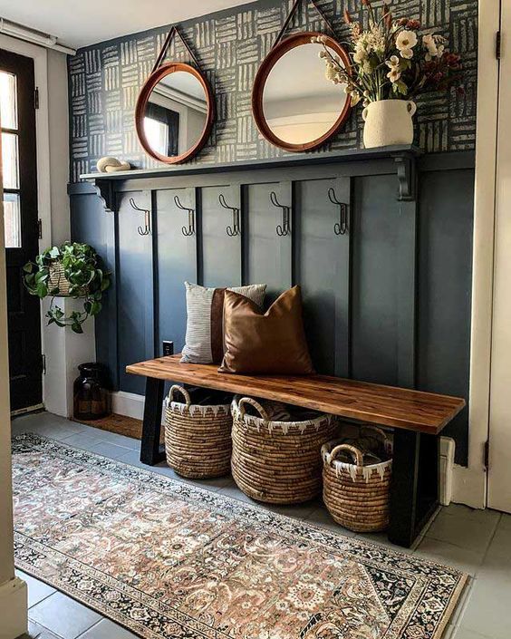 a modern farmhouse entryway with wallpaper, paneling, a bench, baskets and pillows, a duo of mirrors