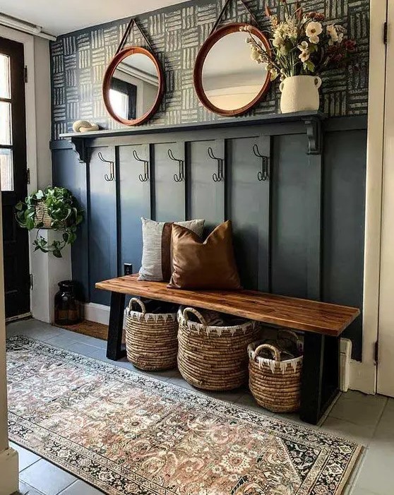 a modern farmhouse hallway with a black paneled wall, a bench, some baskets, potted greenery and blooms and round mirrors