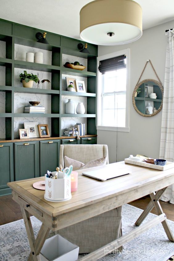 a modern farmhouse home office with a large green storage unit, a whitewashed trestle desk, a neutral chair and a pendant lamp