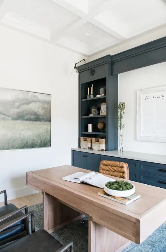a modern farmhouse home office with a navy and white storage unit, a stained desk and leather chairs plus some greenery