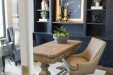 a modern farmhouse home office with a navy storage unit that takes a whole wall, a wooden desk, leather chairs and a refined gold chandelier