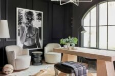 a modern farmhouse home office with black paneled walls, a stained desk, white chairs, a stool, cowhide rugs and a chandelier