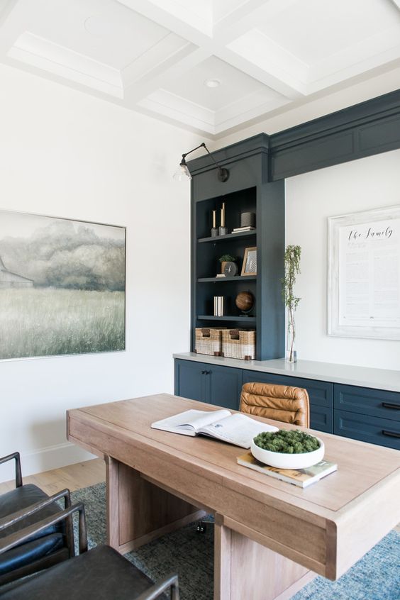 a modern farmhouse home office with built in navy cabinets, a large stained desk, an amber chair and black ones