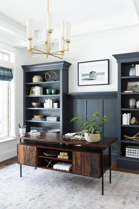 a modern farmhouse home office with soot cabinetry, a dark stained desk, decor, a potted plant and a gold chandelier
