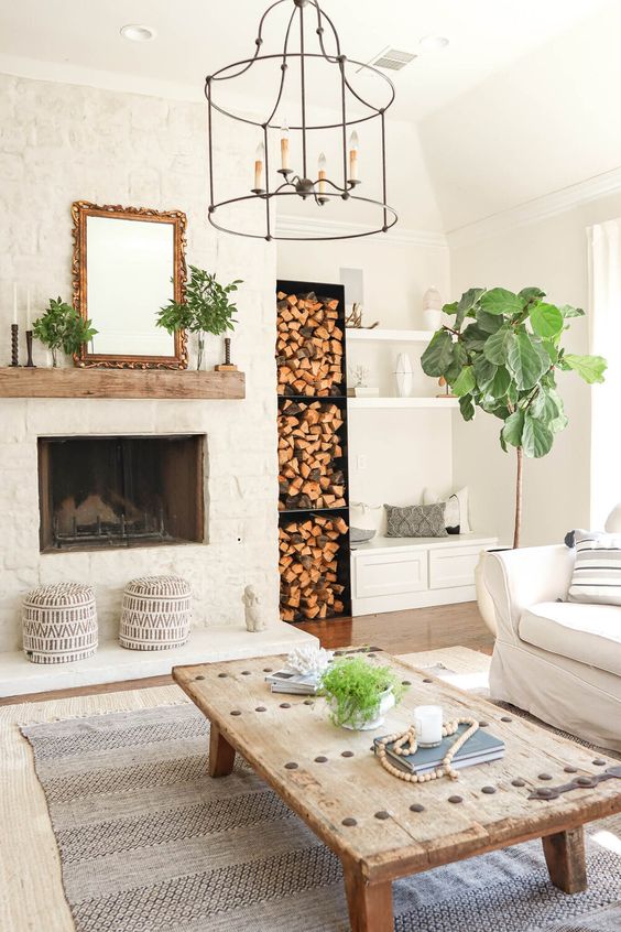 a modern farmhouse living room with a built-in fireplace, firewood storage, open shelves, a white sofa, a coffee table and greenery