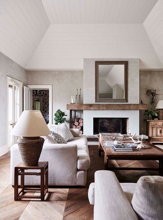 a modern farmhouse living room with a fireplace, firewood storage, a low coffee table, neutral seating furniture, potted plants