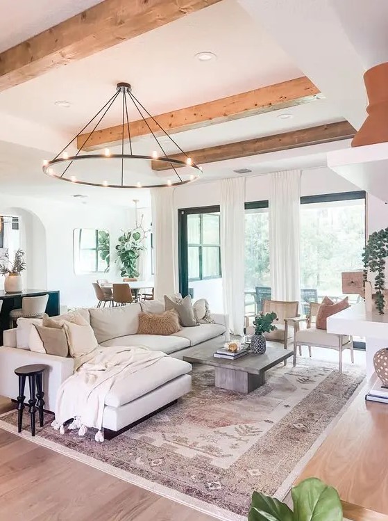 a modern farmhouse living room with wooden beams, a chandelier, a neutral sectional, a coffee table, a fireplace, some chairs