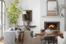 a modern farmhouse living room with wooden beams, a fireplace, a grey sofa, neutral chairs, a coffee table and some greenery