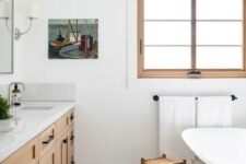 a modern farmhouse meets boho bathroom with a window, a timber vanity, a tub, a stool, a boho rug and some lovely decor